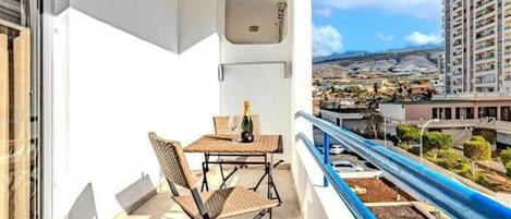 A balcony with a table and chairs, a bottle of champagne, and a view of a cityscape.