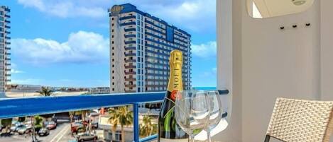 Uma varanda com uma garrafa de champanhe Moët & Chandon e duas taças, com vista para um horizonte urbano que inclui um prédio alto e uma praia.