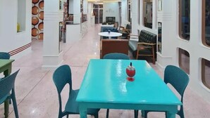 A spacious dining area with a teal table and chairs, a kitchen in the background, and a modern ceiling design with recessed lighting. - Happy Live Quest Hotel  (Bangkok)