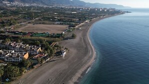 Vista aérea de una zona costera con playa, edificios residenciales y montañas al fondo.