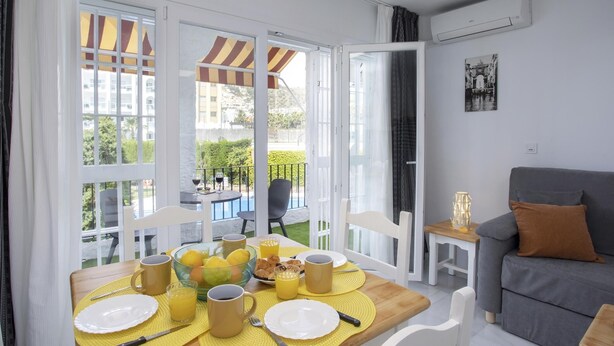 Un comedor con una mesa preparada para el desayuno, un sofá gris y vistas a una piscina.