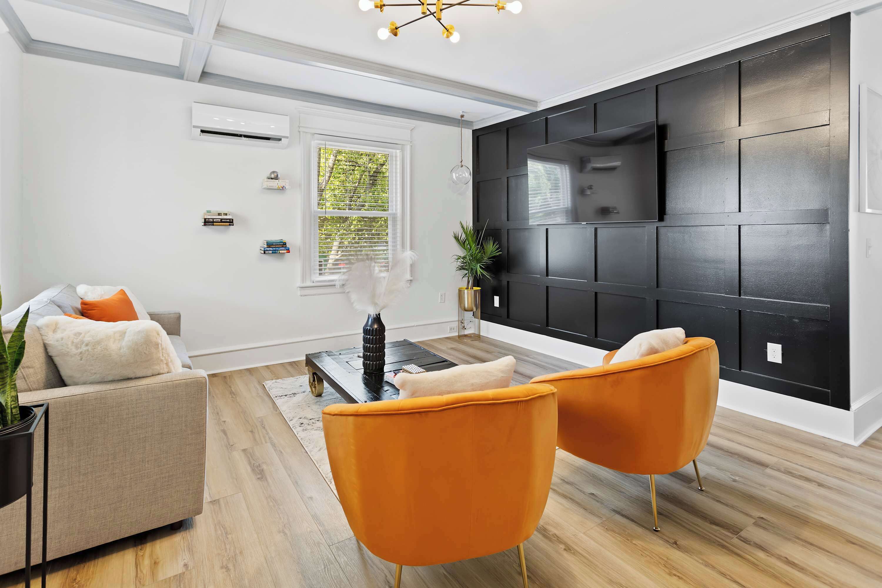 A modern living room with a sofa, two orange chairs, a coffee table, and a black accent wall with a TV.
