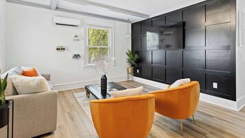 A modern living room with a sofa, two orange chairs, a coffee table, and a black accent wall with a TV.