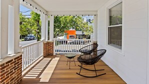 Une véranda en bois avec des balustrades blanches, deux fauteuils à bascule et une petite table.