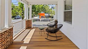 A wooden porch with white railings, two rocking chairs, and a small table.