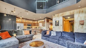 A spacious living room with a large sectional sofa, a coffee table, and a kitchen in the background.