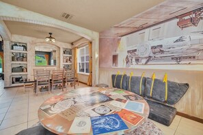 A dining area with a round table covered in papers, a sofa with cushions, and a large mural on the wall.
