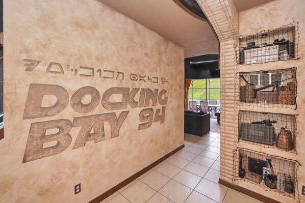 A hallway with a wall displaying 'DOCKING BAY 94' in large letters, a tiled floor, and a netted display of items on the right.