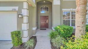 A residential entrance with a garage, a front door, a mailbox, and a small garden with plants and flowers.
