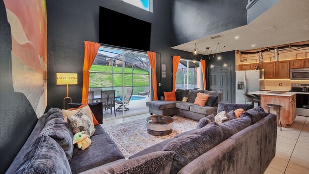 A modern living room with dark sofas, a coffee table, and a view of a backyard.