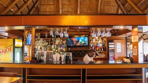 A bar area with a thatched roof, a television screen, and various bottles and glasses. - Galaxy Hotel (Kigali)