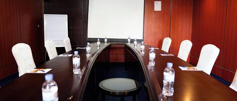 Una sala de conferencias con una larga mesa, sillas blancas y botellas de agua.