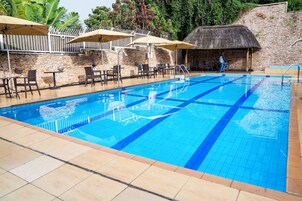 A swimming pool with tiled edges, surrounded by lounge chairs and umbrellas, and a stone wall in the background.