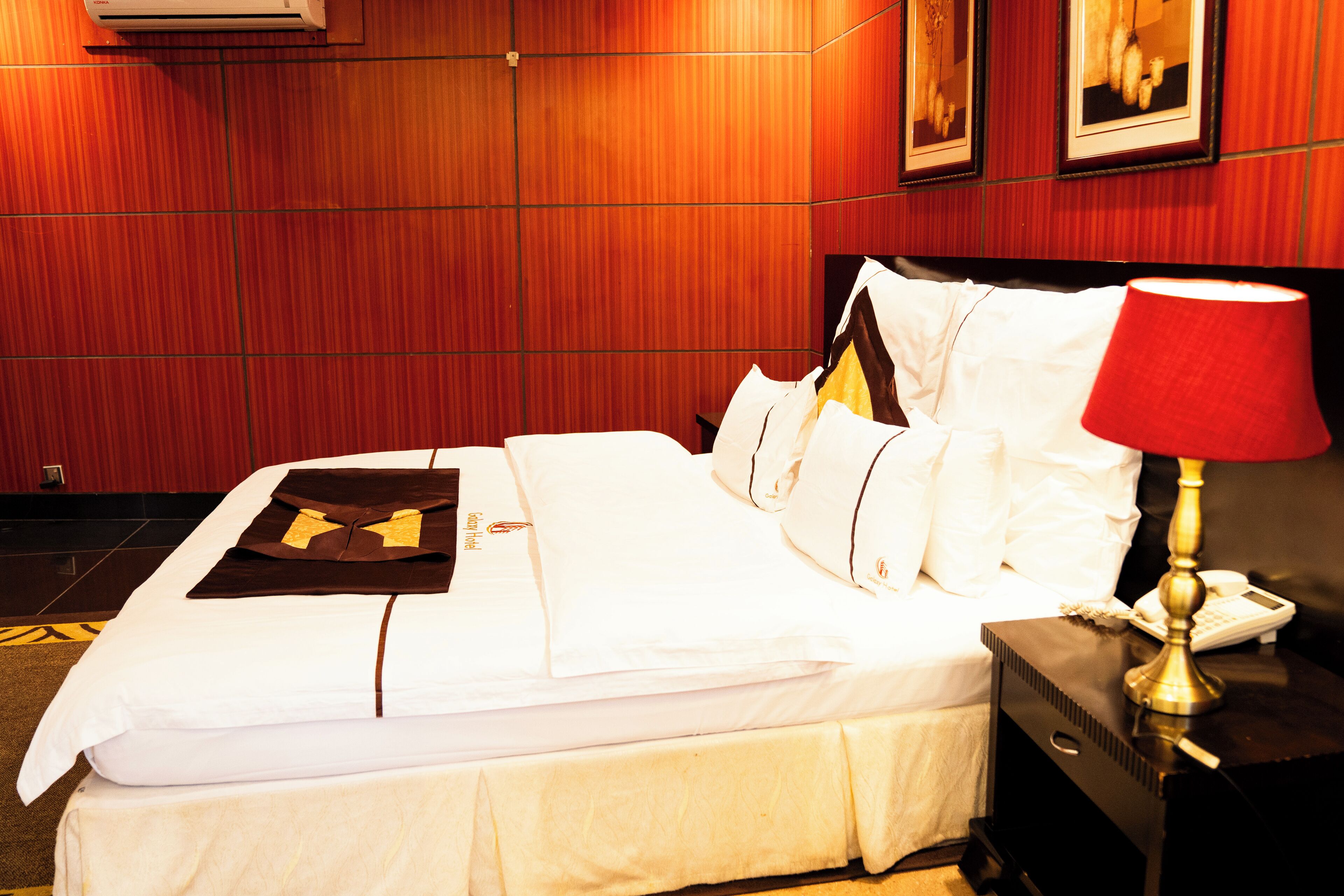 Una habitación de hotel con una cama bien hecha, una mesita de noche con una lámpara y un aire acondicionado instalado en la pared.