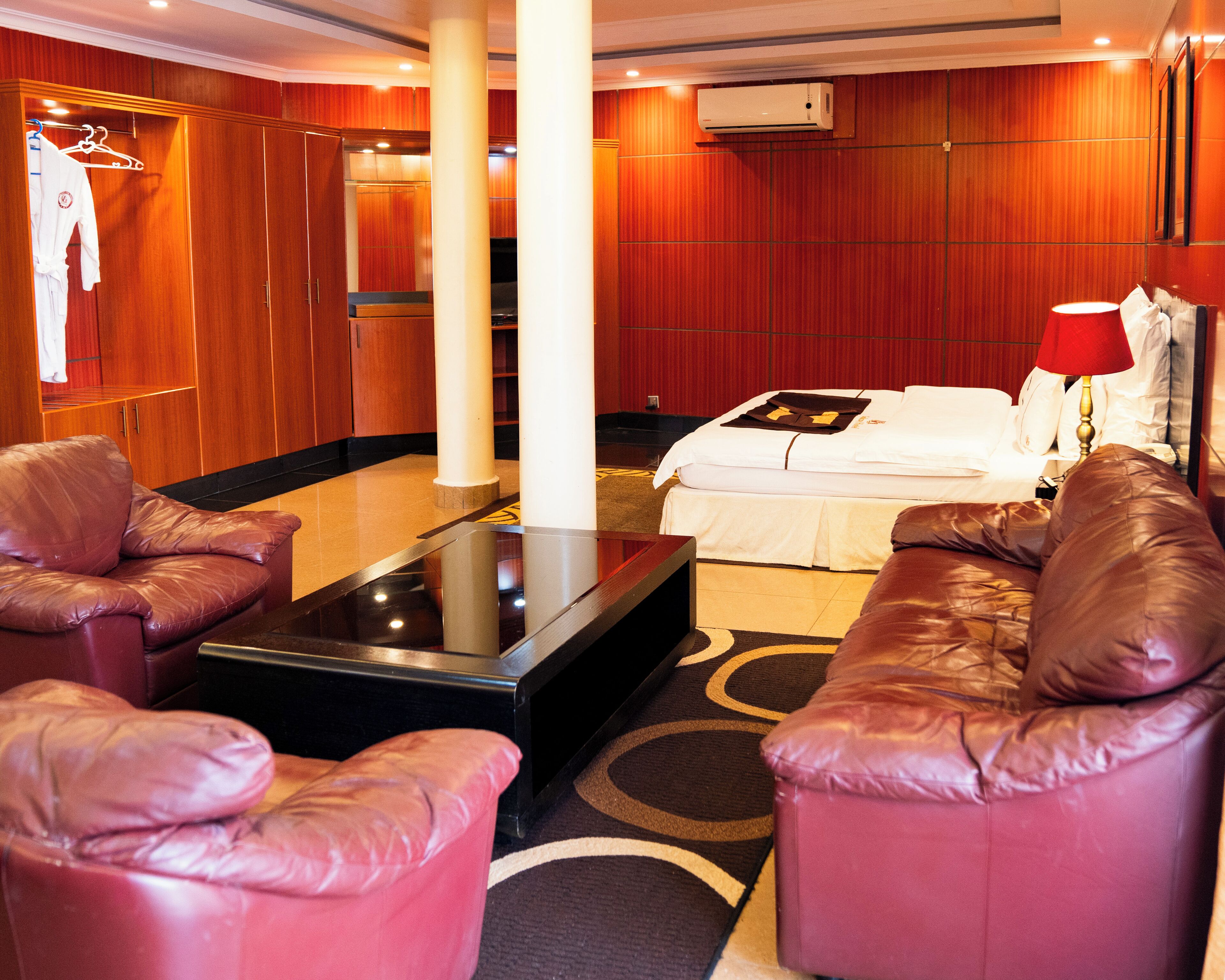 A hotel room with a bed, a red lamp, a coffee table, and leather sofas.