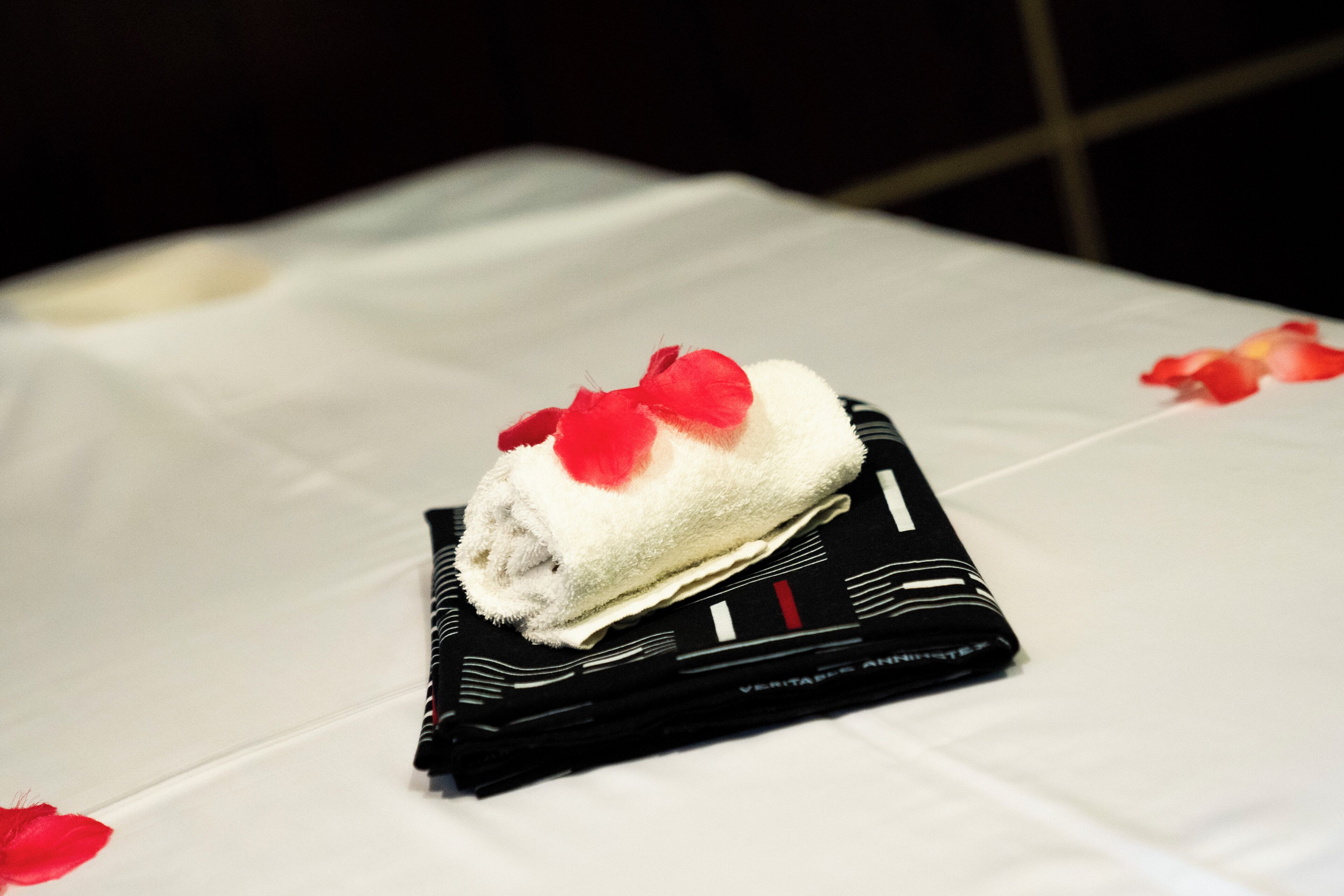 A neatly folded white towel with a red bow on a black pillow on a white tablecloth.