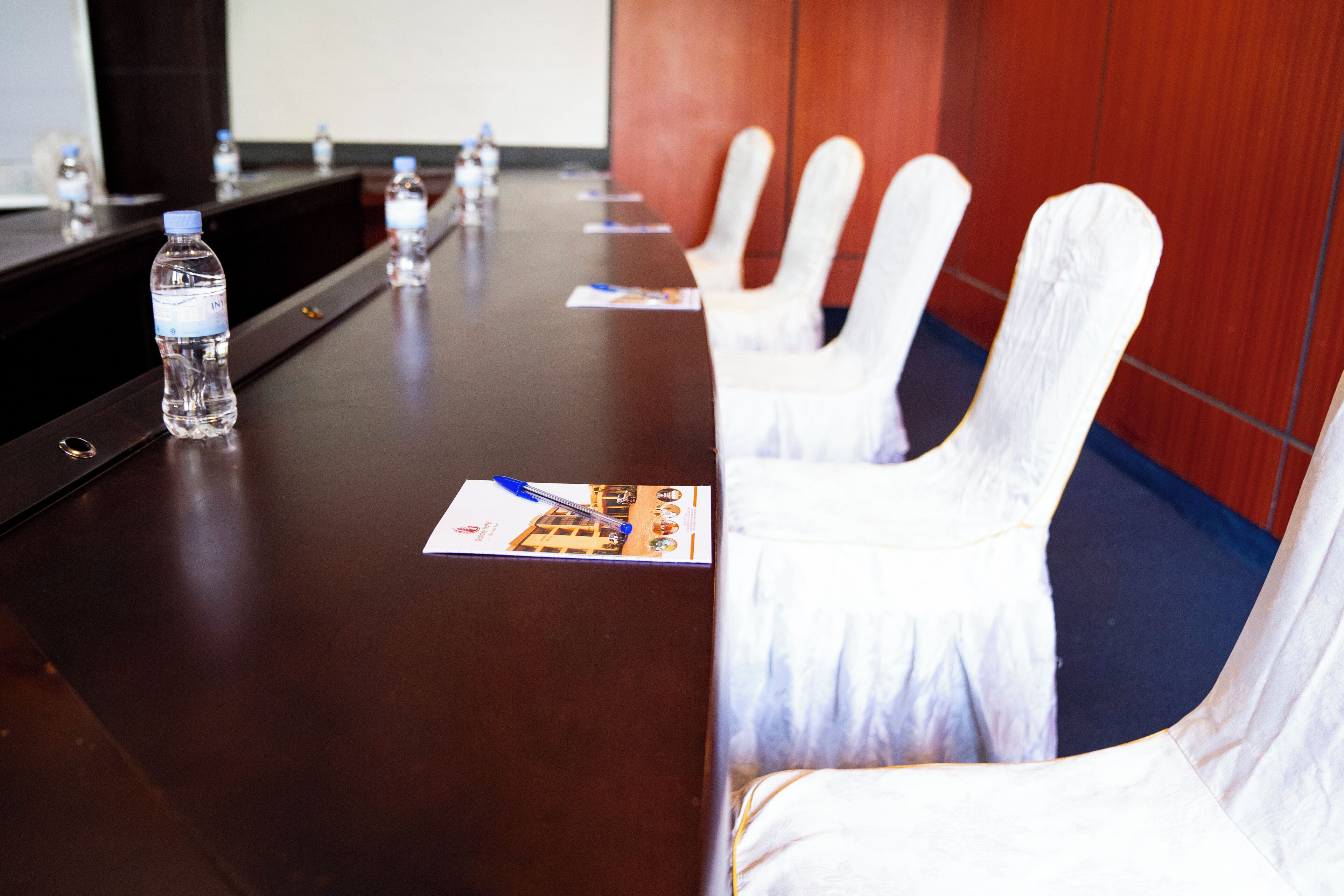 A conference room with a long table, water bottles, name cards, and white chairs.