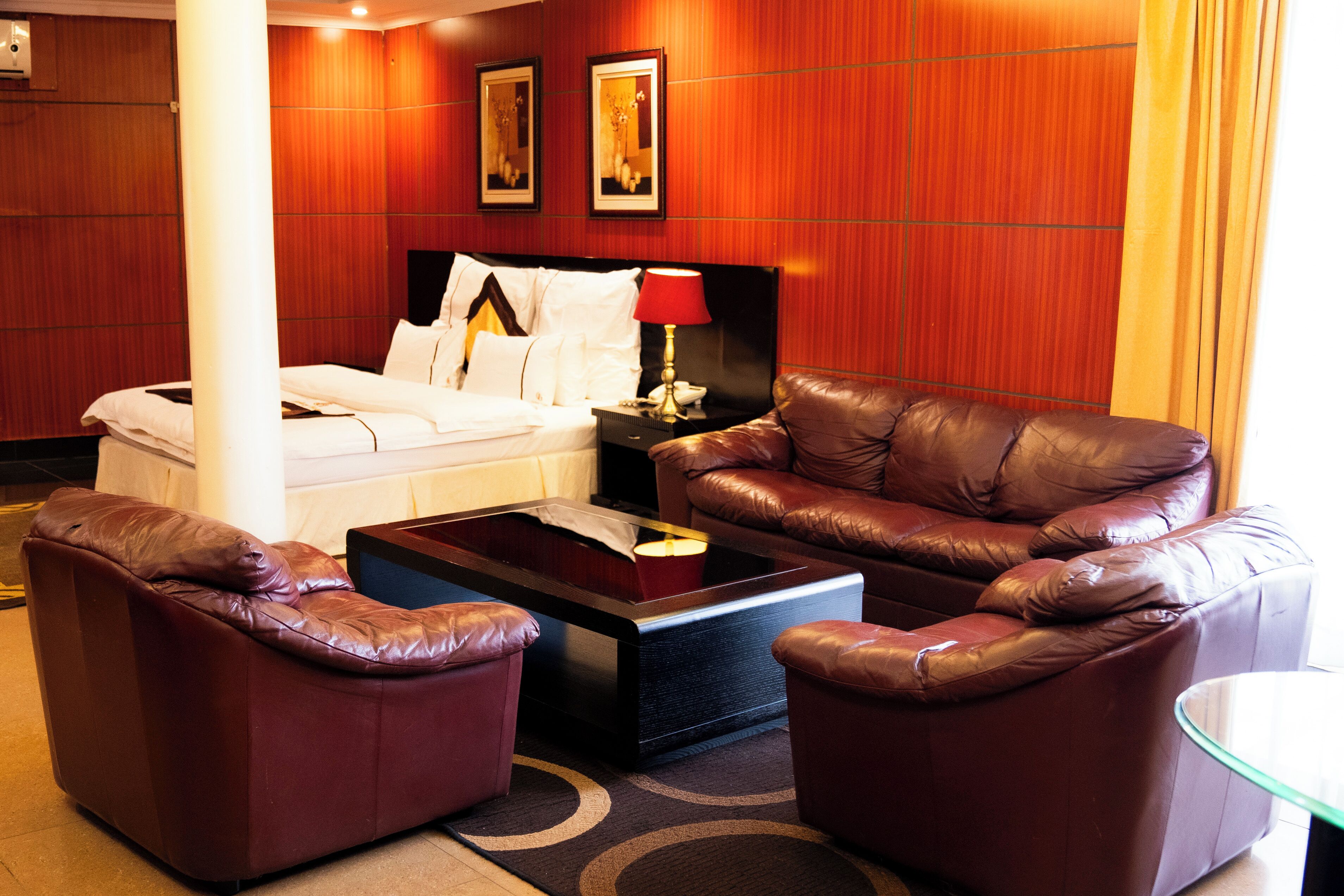 A hotel room with a bed, a leather sofa, a coffee table, and a nightstand with a lamp.