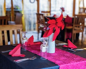 A dining table set with red napkins, clear glassware, and a vase with red flowers. - Galaxy Hotel (Kigali)