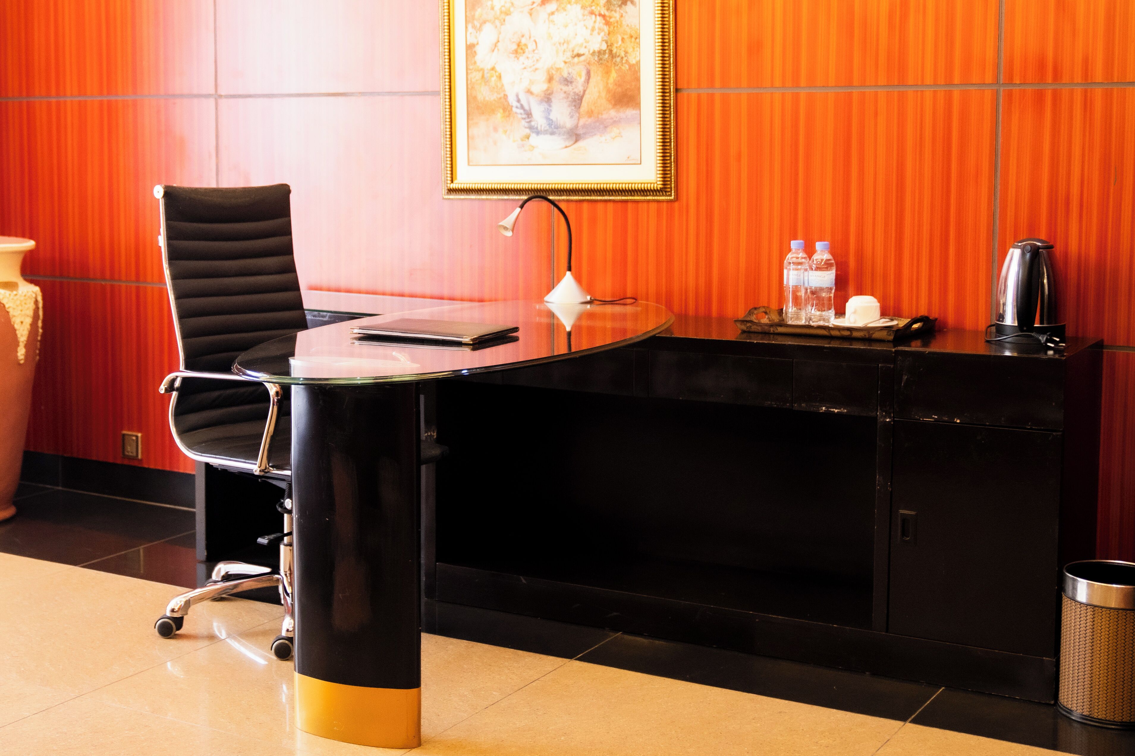 A conference room with a black table, a black chair, a framed picture on the wall, and a small tray with water bottles and a coffee pot.