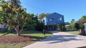 A residential house with a blue exterior, a driveway, and a tree in the front yard. - Palm Grove Cottage Su (Agnes Water)