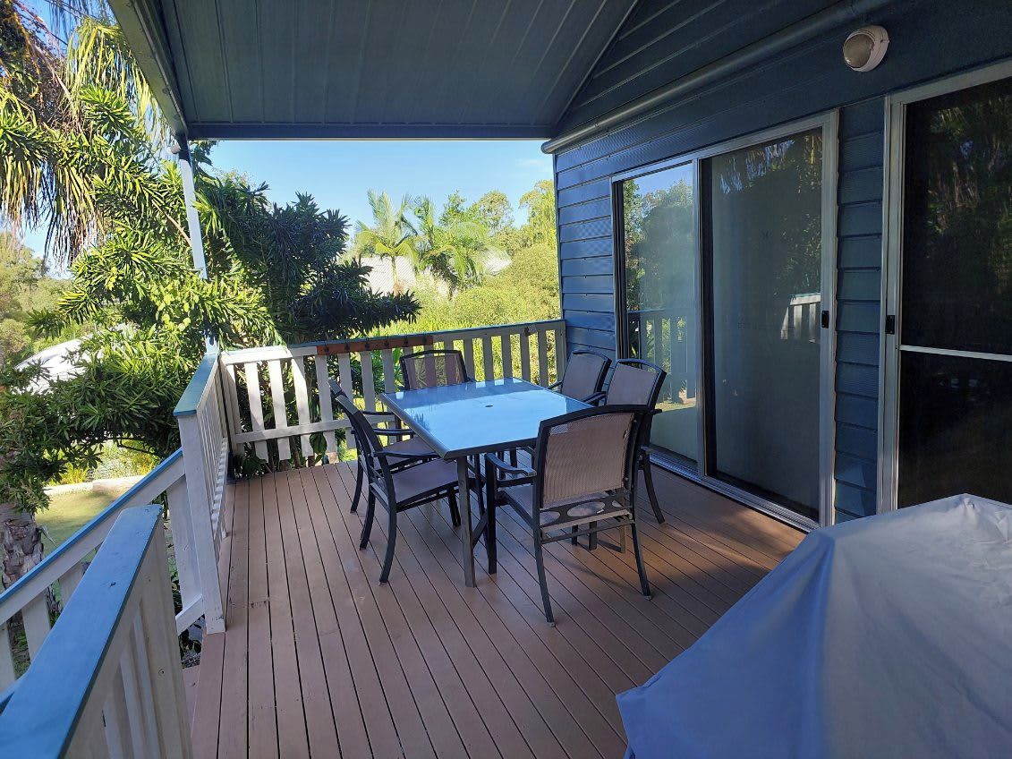 A covered outdoor area with a table and chairs, a sliding glass door, and a view of greenery.