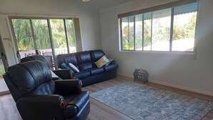 A living room with a black leather sofa, a blue rug, and a wooden floor. - Palm Grove Cottage Su (Agnes Water)
