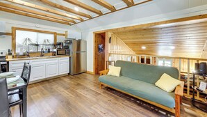 Eine geräumige Küche mit Holzbalken, einem Essbereich mit Tisch und Stühlen sowie einem grünen Sofa mit gelbem Kissen.