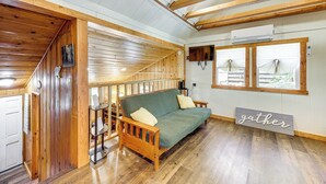 Ein gemütliches Cabin-Interieur mit einer Holztreppe, einem grünen Sofa und einem Schild mit der Aufschrift 'gather'.