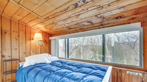 Una habitación de cabaña de madera con una cama, una ventana y una lámpara fijada a la pared.