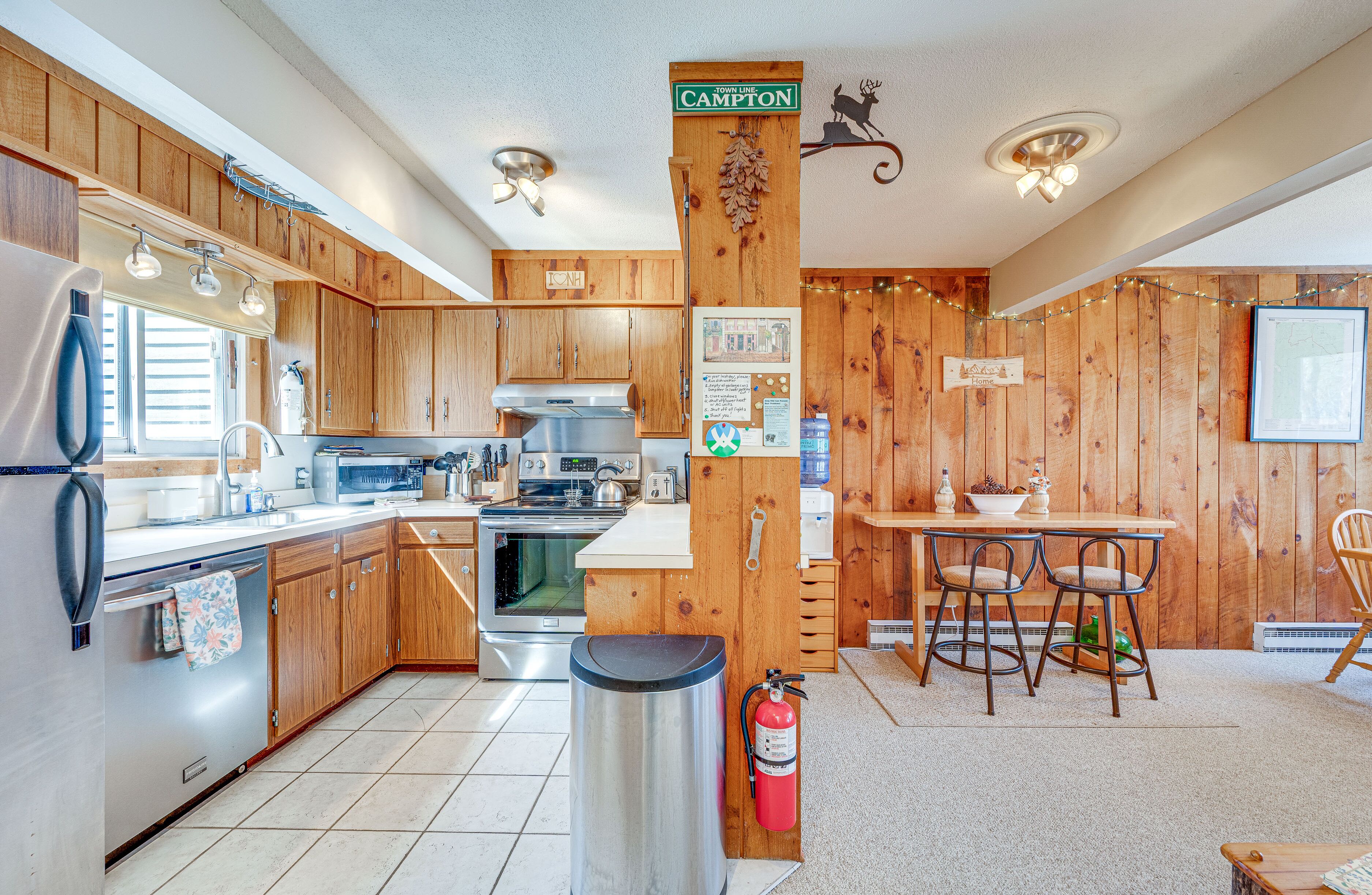 A kitchen with wooden cabinets, stainless steel appliances, a dining area with two chairs, and a fire extinguisher.