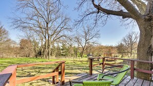 Un terrazzo in legno con sedie verdi e una ringhiera di legno che si affaccia su un parco erboso con alberi.