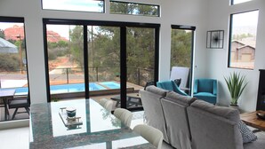 A modern living room with a glass-top dining table, grey sofa, and a view of a swimming pool and red rock landscape. - 2 King Ensuites Elevated Views Spa Amenities at Sedona Sky (Sedona)