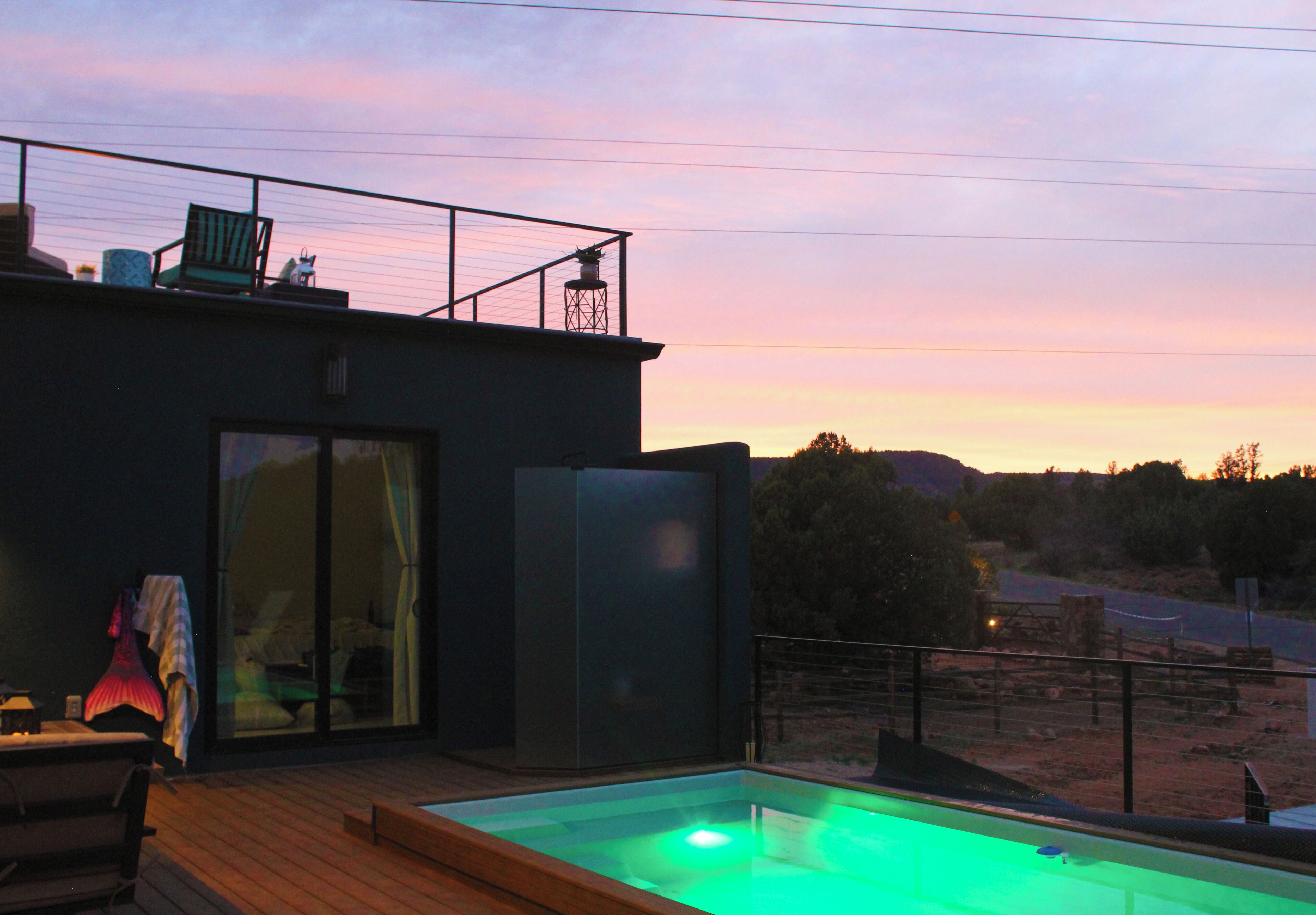 Un bâtiment moderne doté d’une porte en verre, d’une piscine éclairée de lumières vertes et d’une terrasse aménagée avec du mobilier d’extérieur.