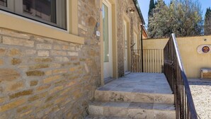 A stone building with a staircase leading to a door, a metal gate, and a wall with a decorative emblem. - Borgo Ariano 2 – Apartment with pool (Volterra)