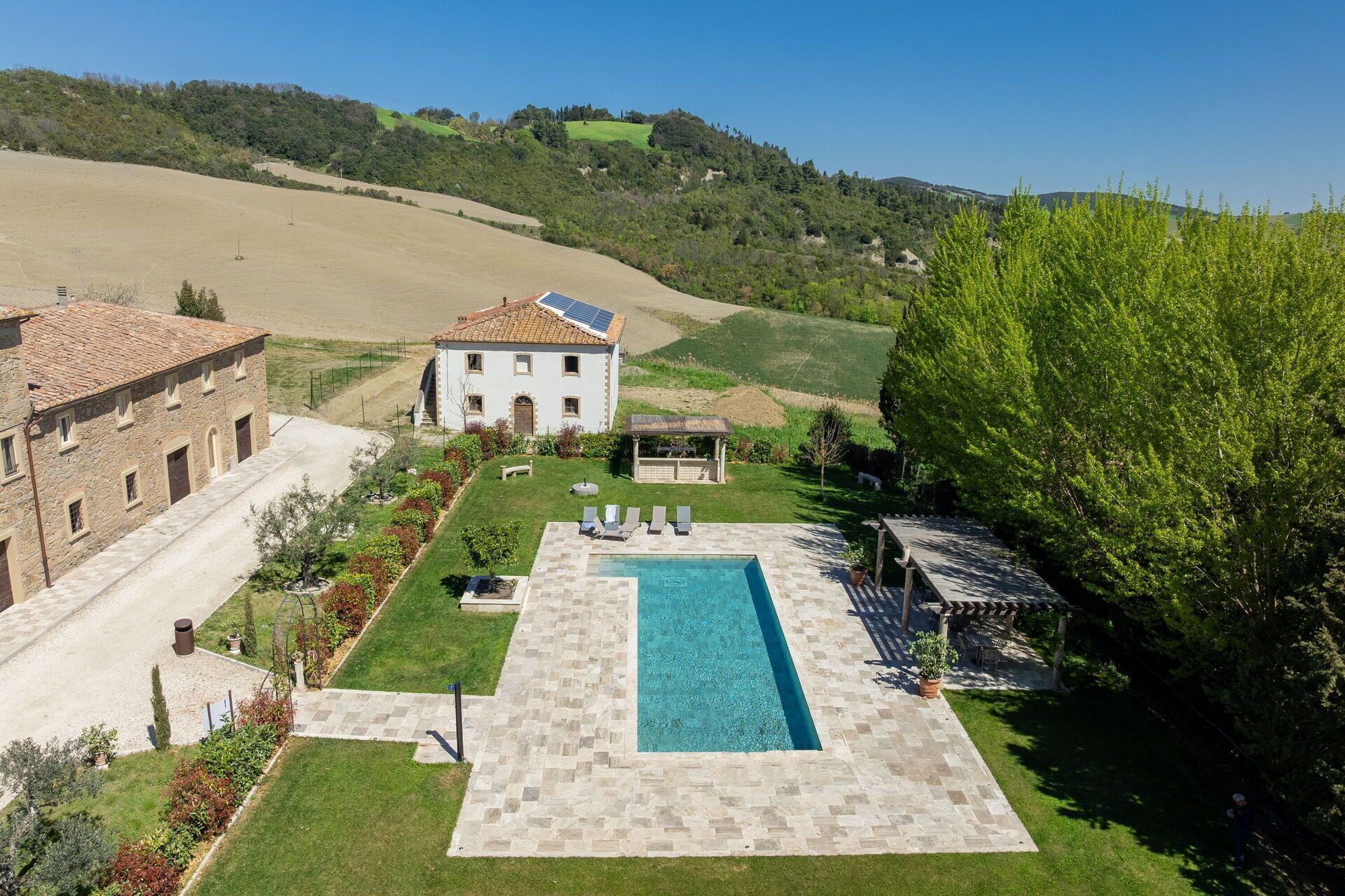 A villa with a swimming pool, surrounded by a well-maintained lawn and a view of rolling hills.
