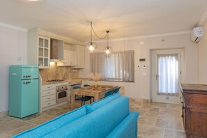 A compact kitchen with a teal refrigerator, a wooden dining table, and a blue sofa.