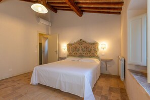 Ein Schlafzimmer mit einem Bett, zwei Nachttischlampen, einer Klimaanlage, einer Holzbalkendecke und einer Tür.