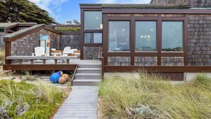 Ein modernes Haus mit einer Holzterrasse, Sitzgelegenheiten im Freien und einem großen Fenster mit Blick auf die Landschaft.