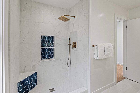 A modern bathroom with a shower, a small window with blue patterned glass, and a towel rack with white towels.