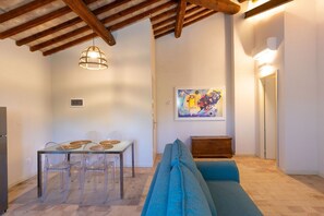 Un espace repas comprenant une table et des chaises, un canapé, un tableau accroché au mur et un plafond avec des poutres apparentes.