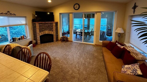 A living room with a fireplace, a dining area, and a view through glass doors to an outdoor patio. - Seaside Paradise at Sebastian Shores (Gold Beach)