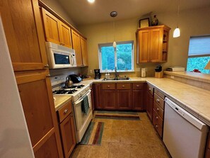 A compact kitchen with wooden cabinets, a microwave, a stove, a sink, and a dishwasher.