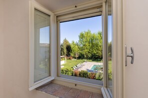 Una puerta corrediza de vidrio da a un patio trasero con piscina, rodeado de follaje y un cielo despejado.