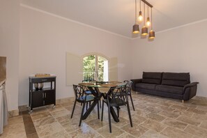 Un comedor con mesa de vidrio, sillas negras, un sofá oscuro y una zona de cocina con armarios y encimera.