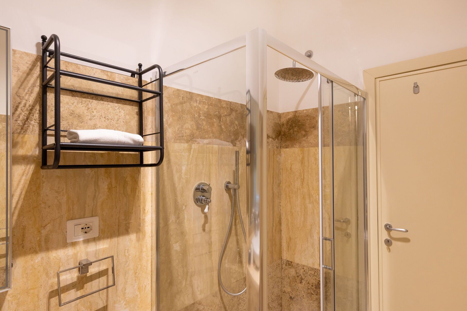 A bathroom with a glass shower enclosure, a towel rack, and a door.