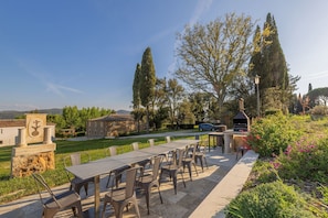 Patio esterno con tavolo e sedie, barbecue e un edificio in pietra con una bandiera.
