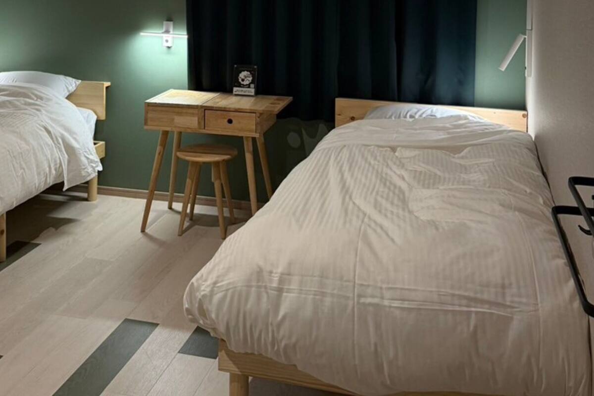 Ett hotellrum med två separata sängar, ett skrivbord i trä och en liten pall.