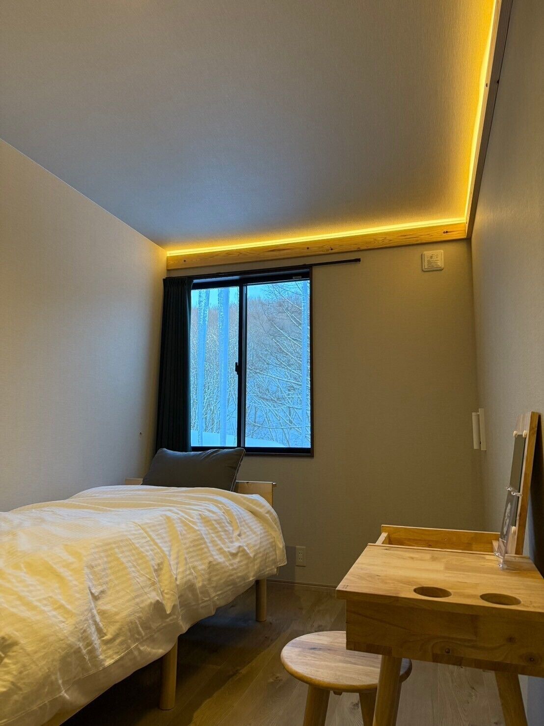 A bedroom with a bed, a desk, and a window with a view of trees.