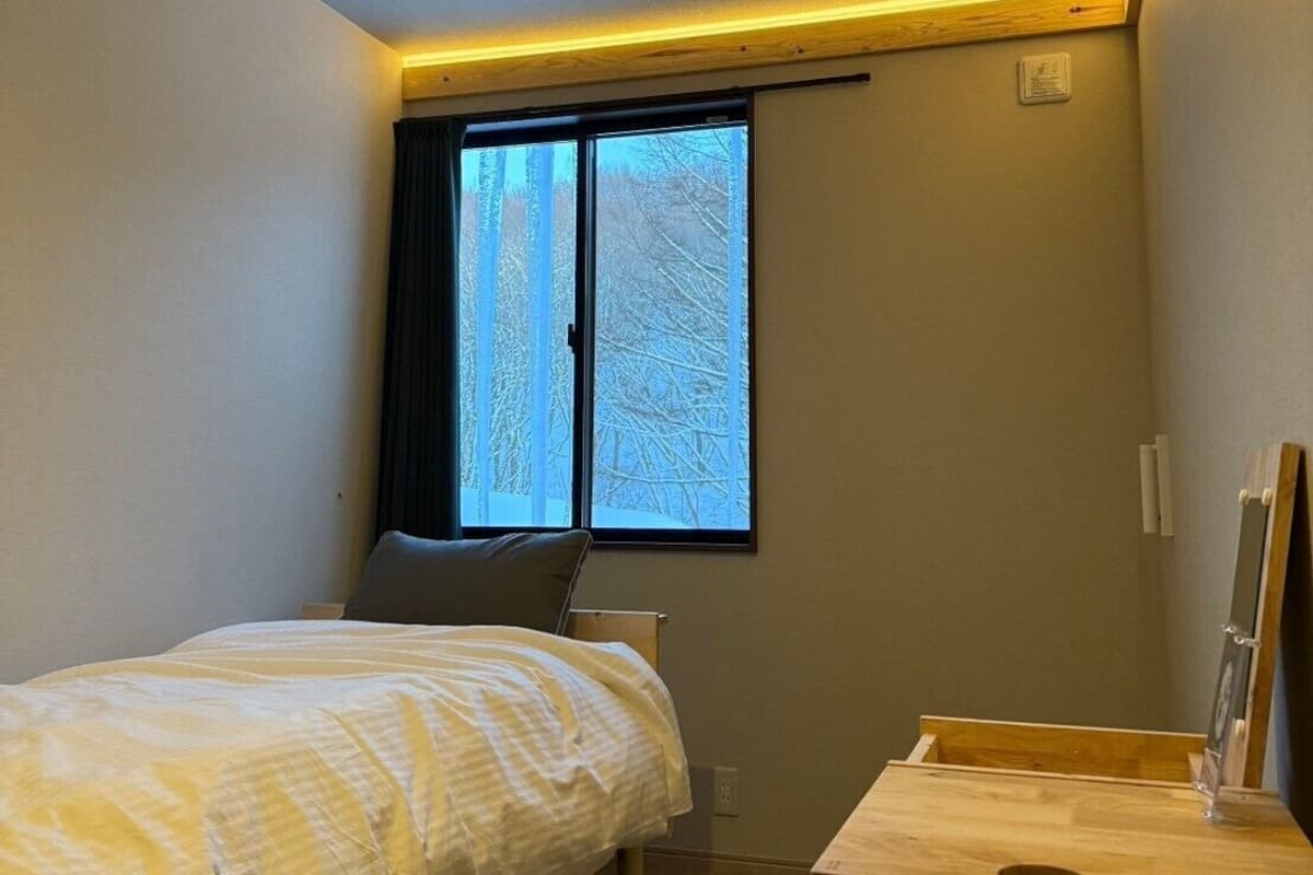 A bedroom with a bed, a desk, and a window with a view of trees.